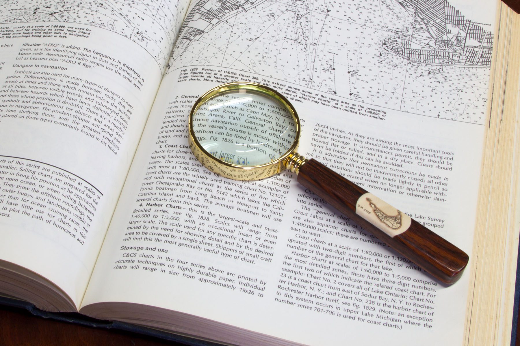 Scrimshaw magnifying glass resting on nautical chart reference book