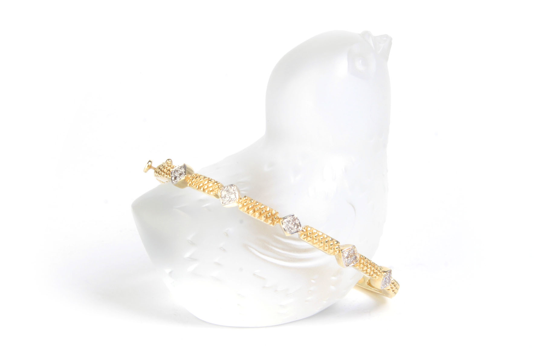Diamond and gold bracelet resting on a translucent bird statue